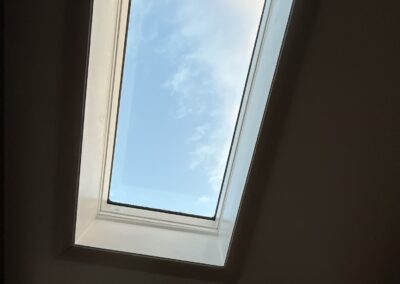 Rectangular skylight window in a ceiling showing a view of the blue sky with some clouds.