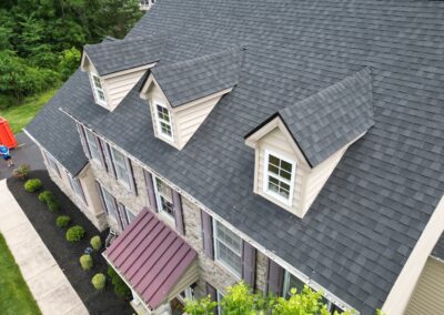 Aerial view of a two-story house with stone and siding exterior, featuring three dormer windows and a dark gray shingled roof.