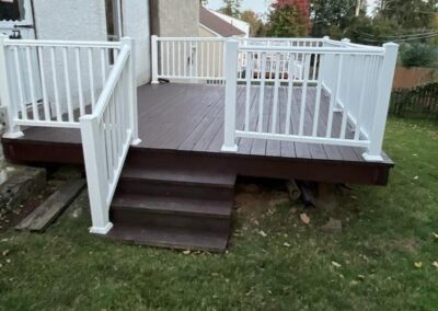 A wooden deck with white railings and three steps leads from a house to a grassy backyard.
