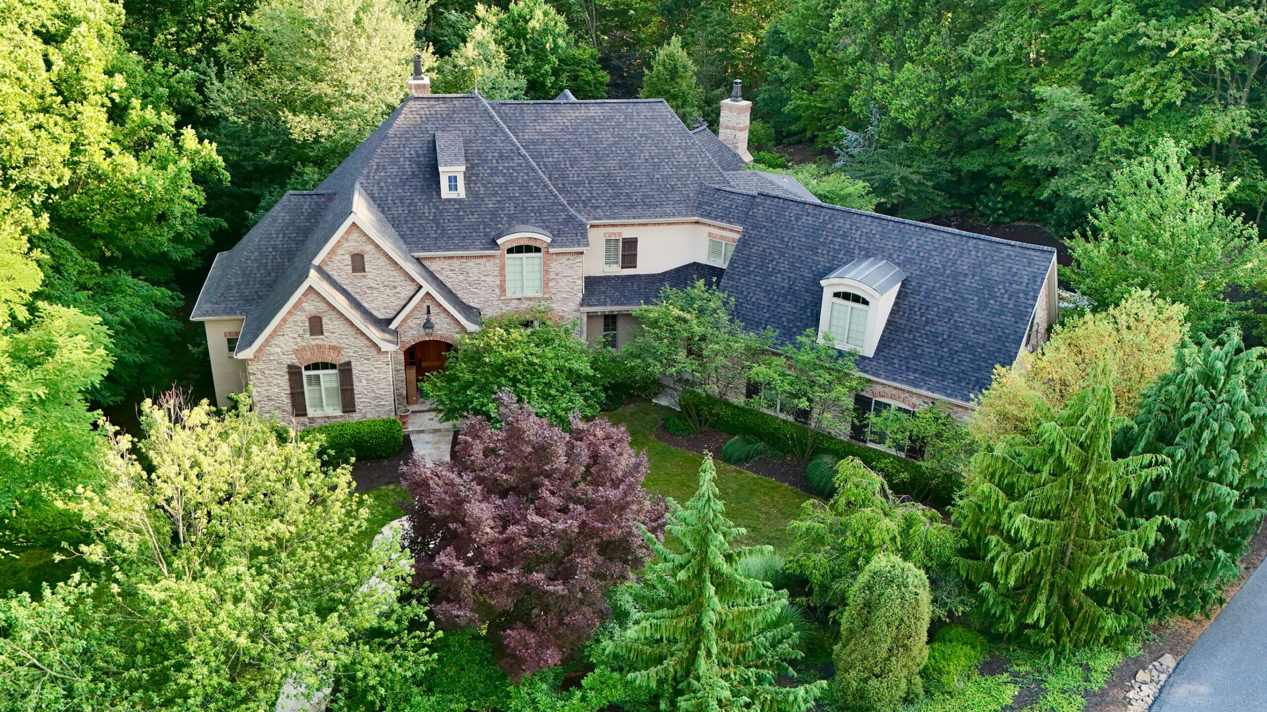 Aerial shot of large house with focus on roof, surrounded by trees 